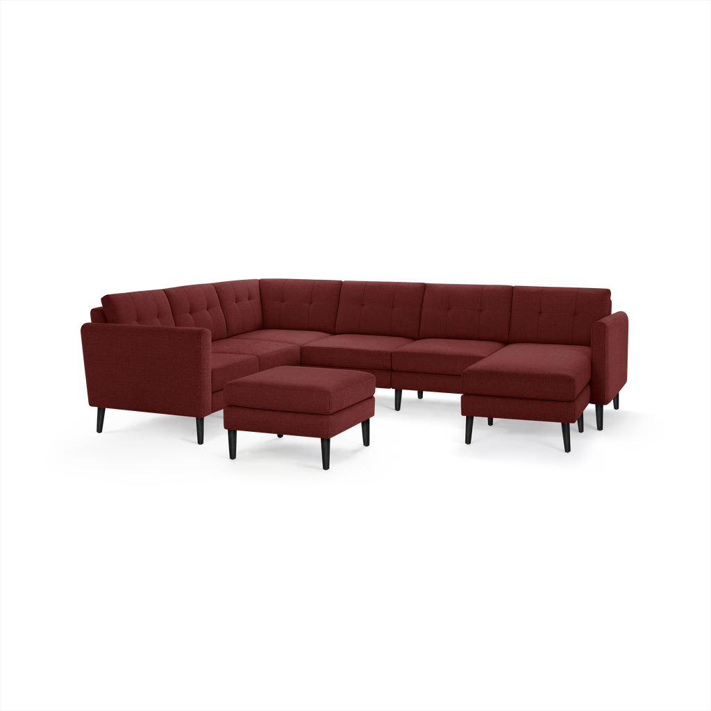Modern sectional sofa in dark red fabric with tufted back cushions, black tapered legs, and matching ottoman.