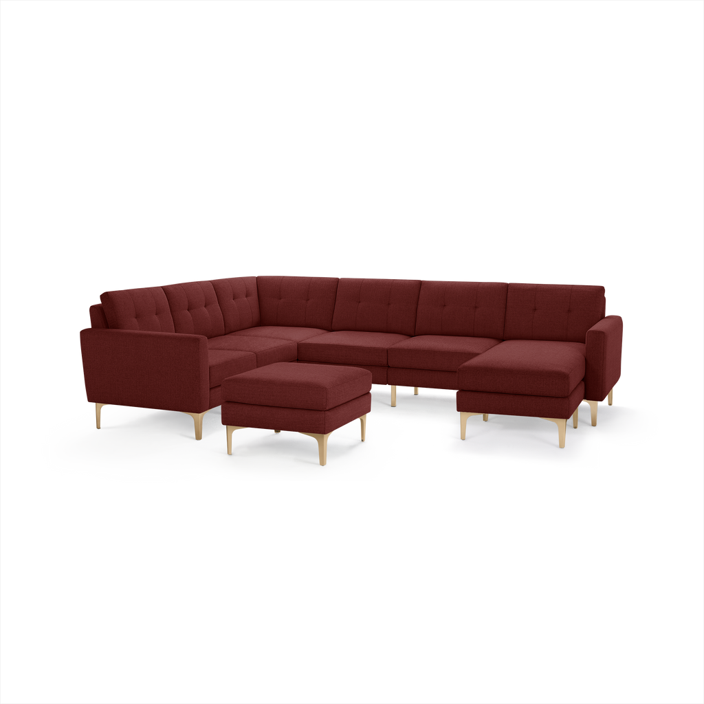 Modern L-shaped sectional sofa in deep burgundy fabric with tufted back cushions and light wooden legs, accompanied by a matching ottoman.