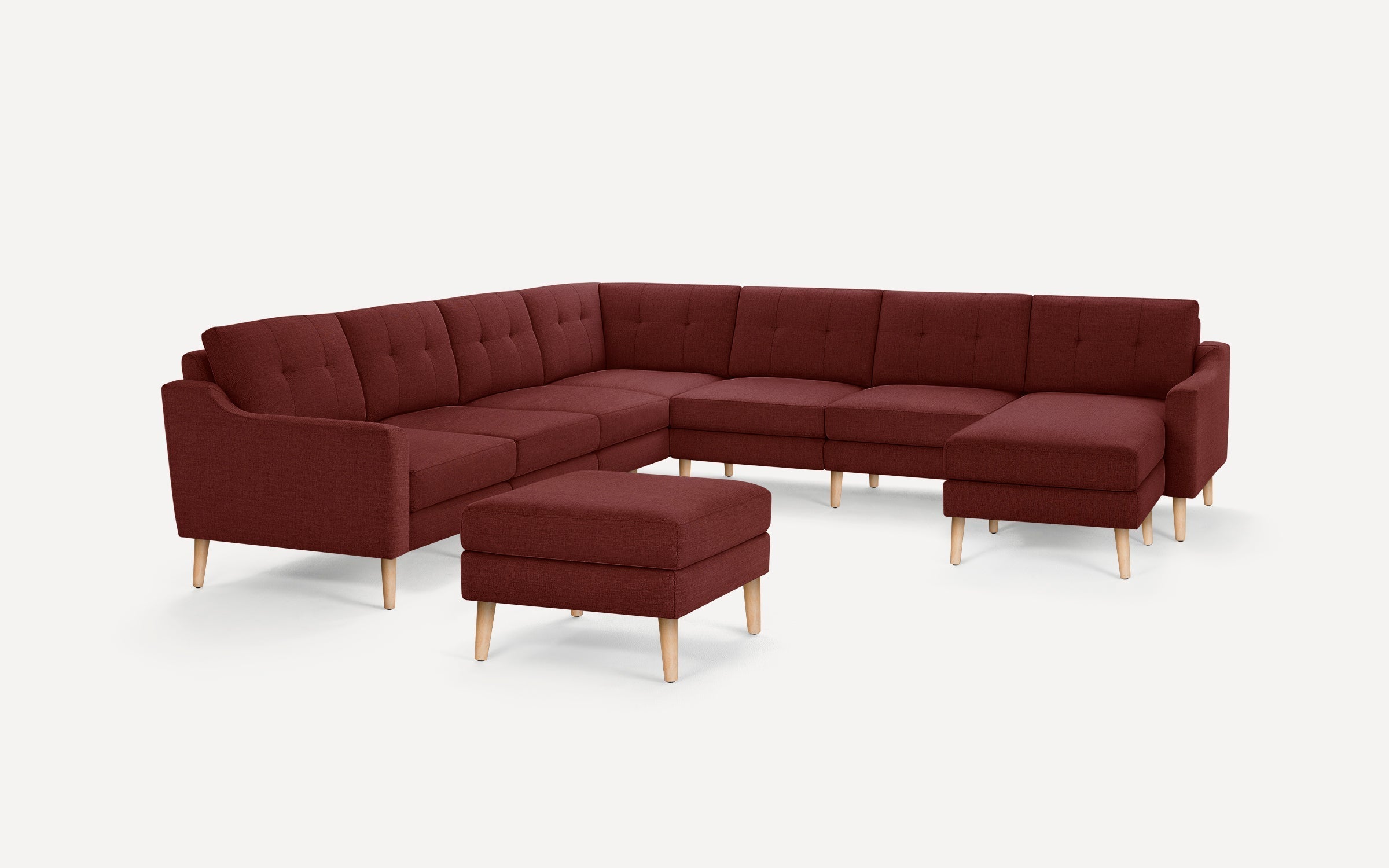 Large L-shaped sectional sofa in deep red fabric with tufted cushions and light wooden legs, accompanied by a matching rectangular ottoman.