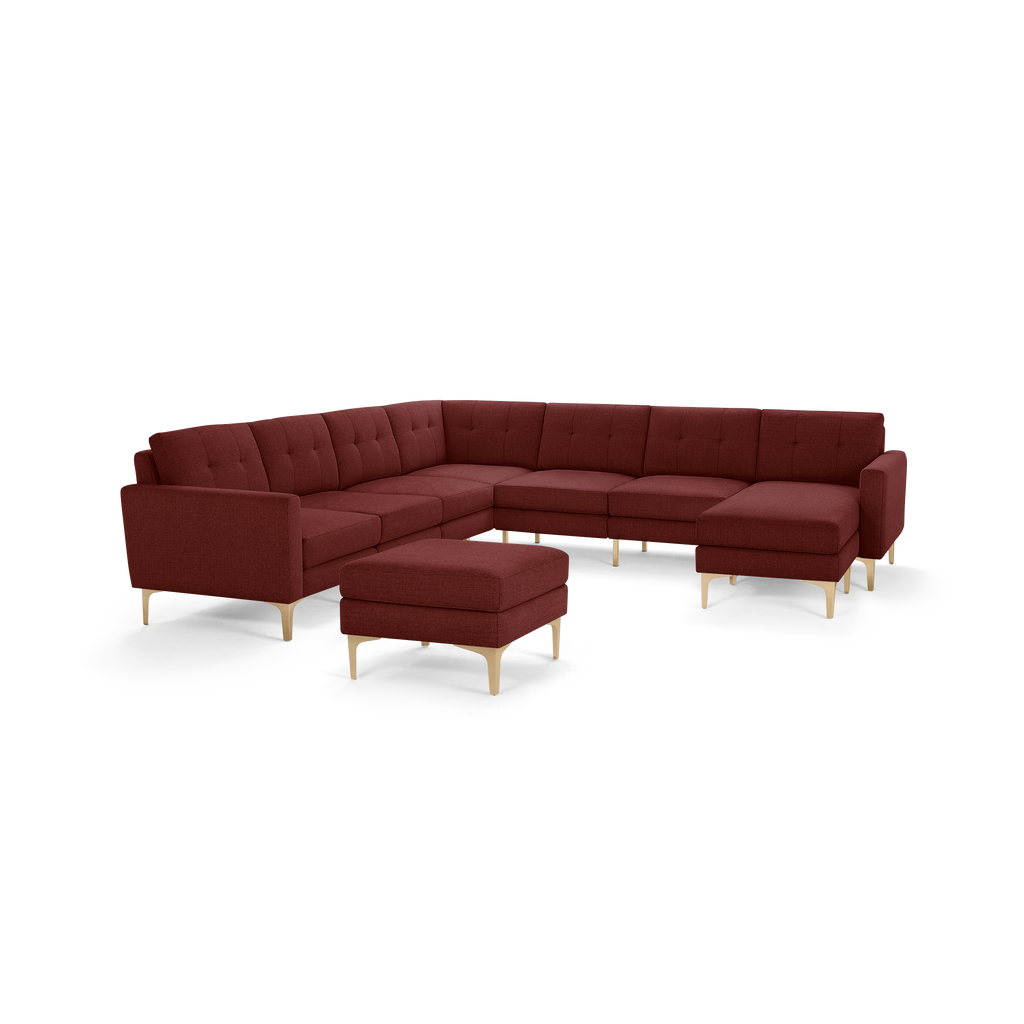 Large U-shaped sectional sofa in rich burgundy fabric with tufted back cushions and light wood legs, including a matching ottoman.