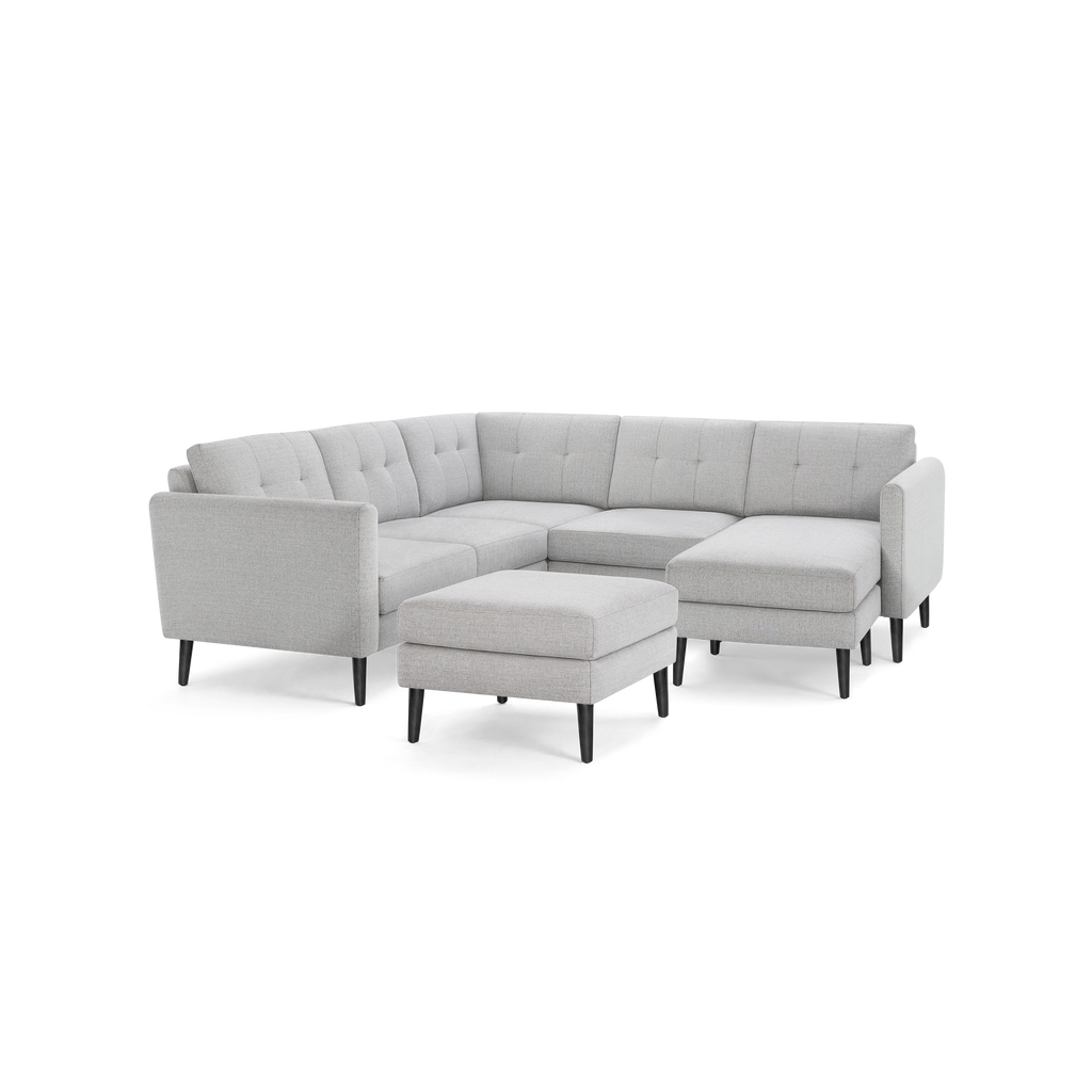 Light gray modern sectional sofa with tufted cushions, three-seater design, chaise lounge, and matching ottoman on black tapered legs.