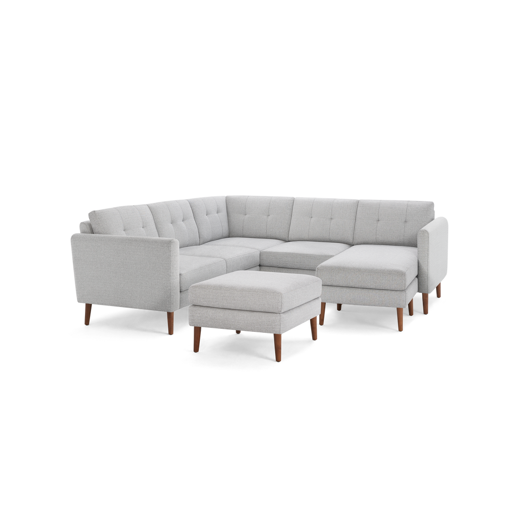 Light gray fabric sectional sofa with tufted back cushions, wooden legs, and matching ottoman on black background.