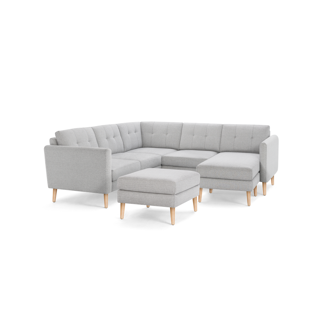 Gray L-shaped sectional sofa with tufted cushions, wooden legs, and a matching ottoman, modern and stylish design.