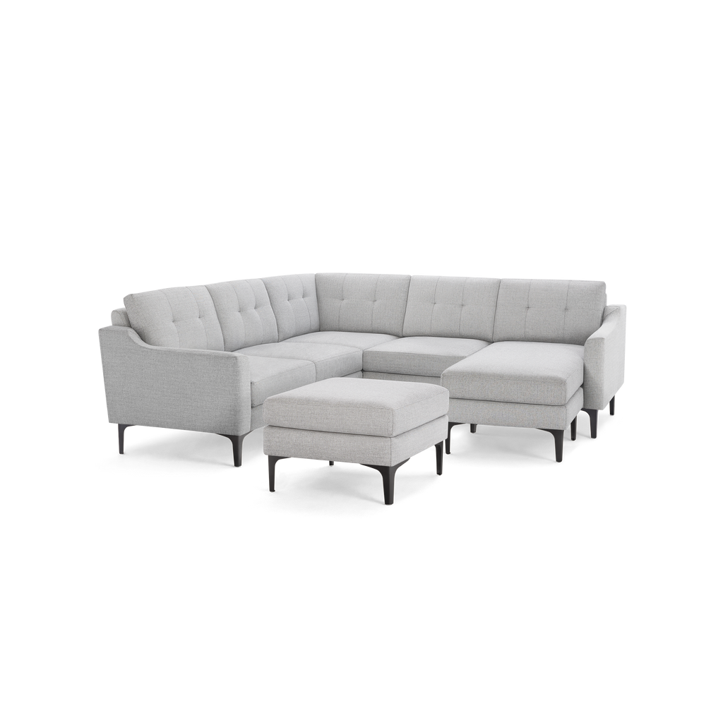 Light gray L-shaped sectional sofa with tufted cushions and matching ottoman, featuring slim black legs.