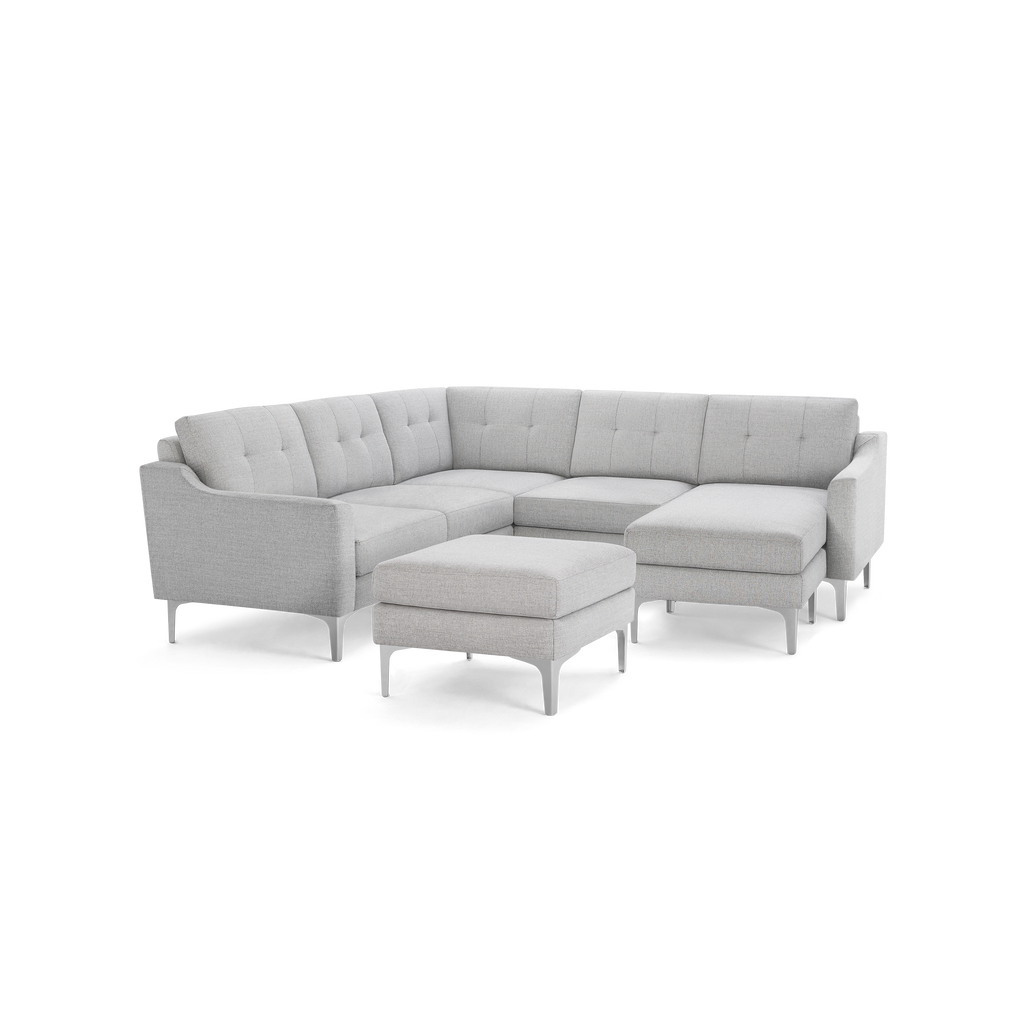 Light gray modern sectional sofa with tufted back cushions, metal legs, and matching ottoman on dark background.