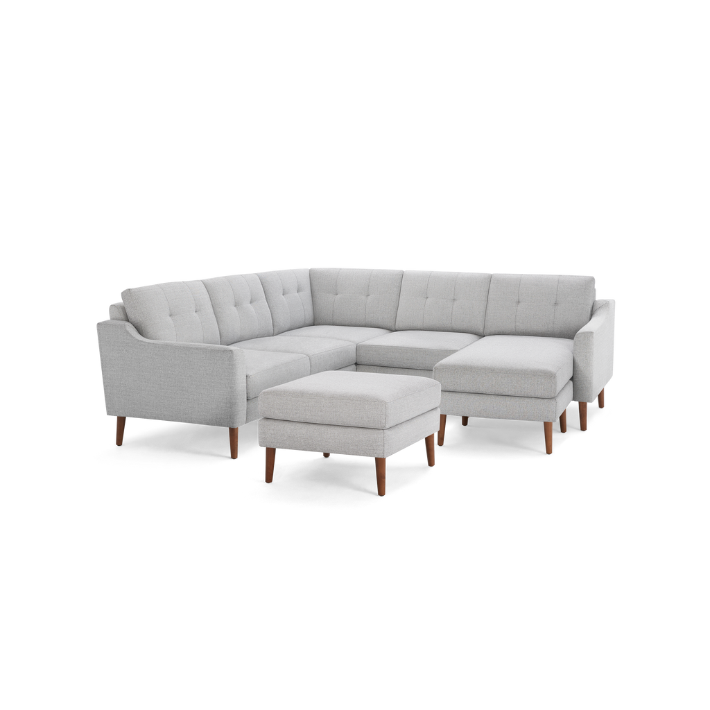 Light gray fabric sectional sofa with tufted cushions, wooden legs, and matching ottoman, showcasing a modern L-shaped design.