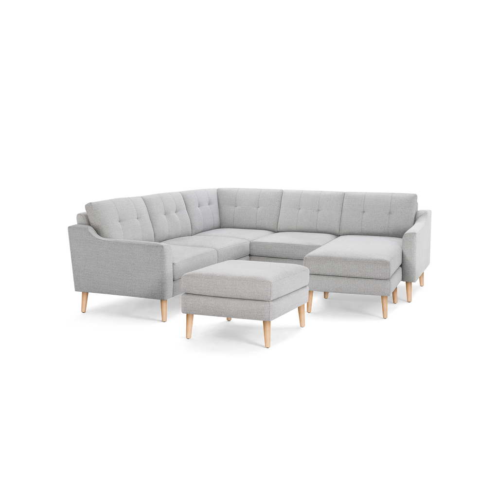 Light gray fabric sectional sofa with tufted cushions, wooden legs, and matching ottoman against black background.