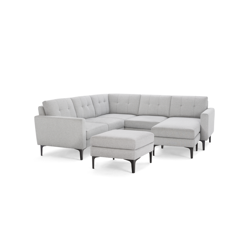 Light gray fabric upholstered L-shaped sectional sofa with tufted back cushions and matching ottoman on black slender legs.
