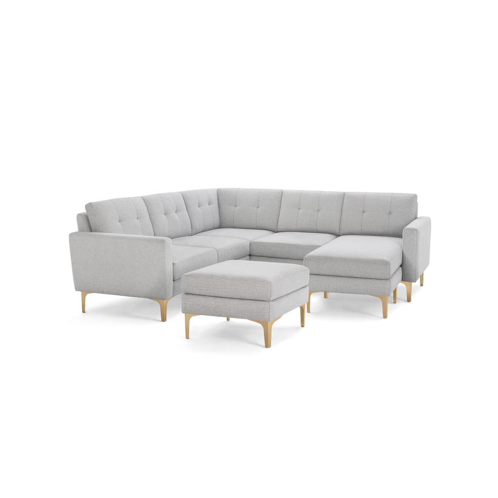 Light gray fabric sectional sofa with tufted back cushions, wooden legs, and a matching ottoman on a black background.