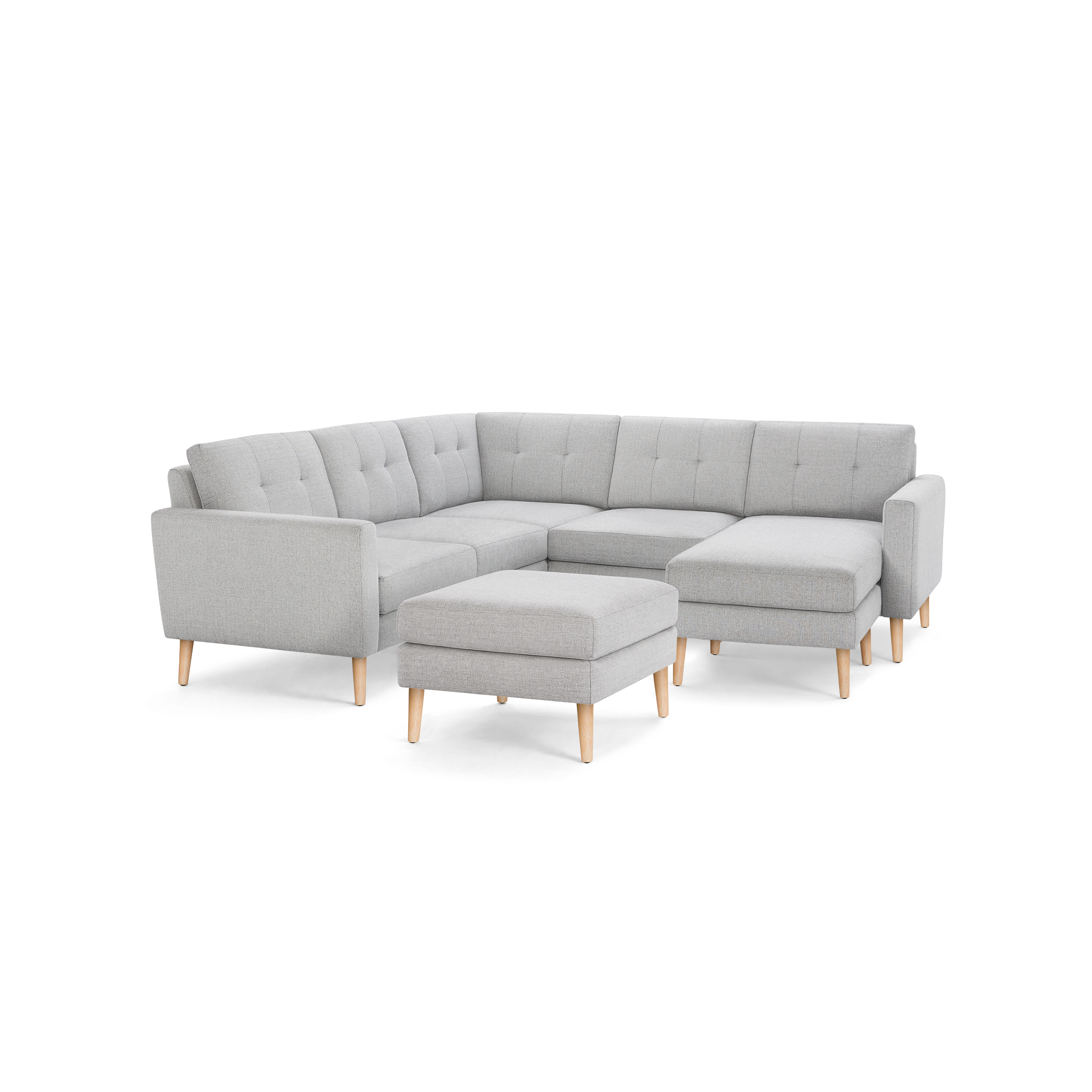 Light gray fabric sectional sofa with tufted back cushions, wooden legs, and matching ottoman, isolated on black background.