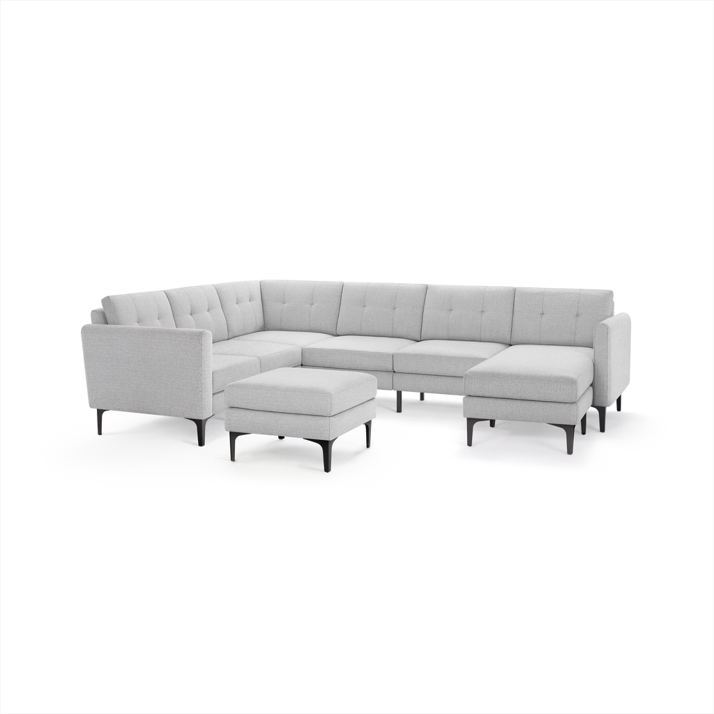 Light gray modern sectional sofa with tufted back cushions and matching ottoman, supported by sleek black legs.