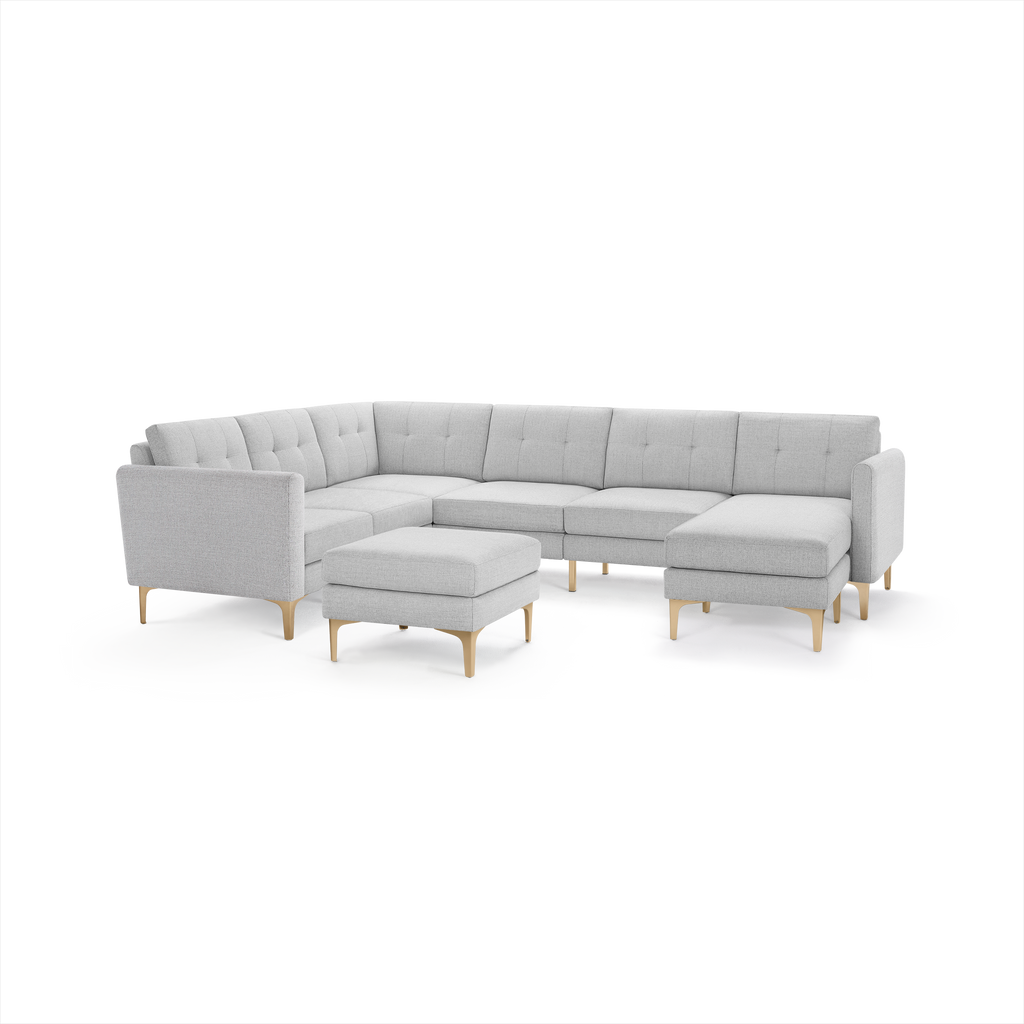 Light gray upholstered sectional sofa with tufted back cushions, wooden legs, chaise lounge, and matching square ottoman.