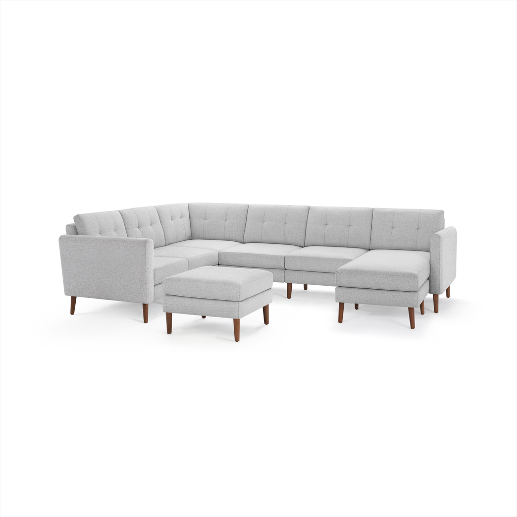 Light gray fabric sectional sofa with tufted back cushions, wooden legs, and matching ottoman, arranged in an L-shape.