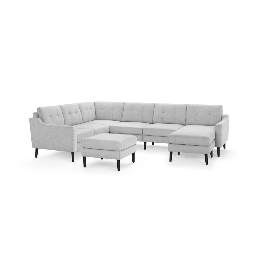 Light gray L-shaped sectional sofa with tufted back cushions, black wooden legs, and matching ottoman.