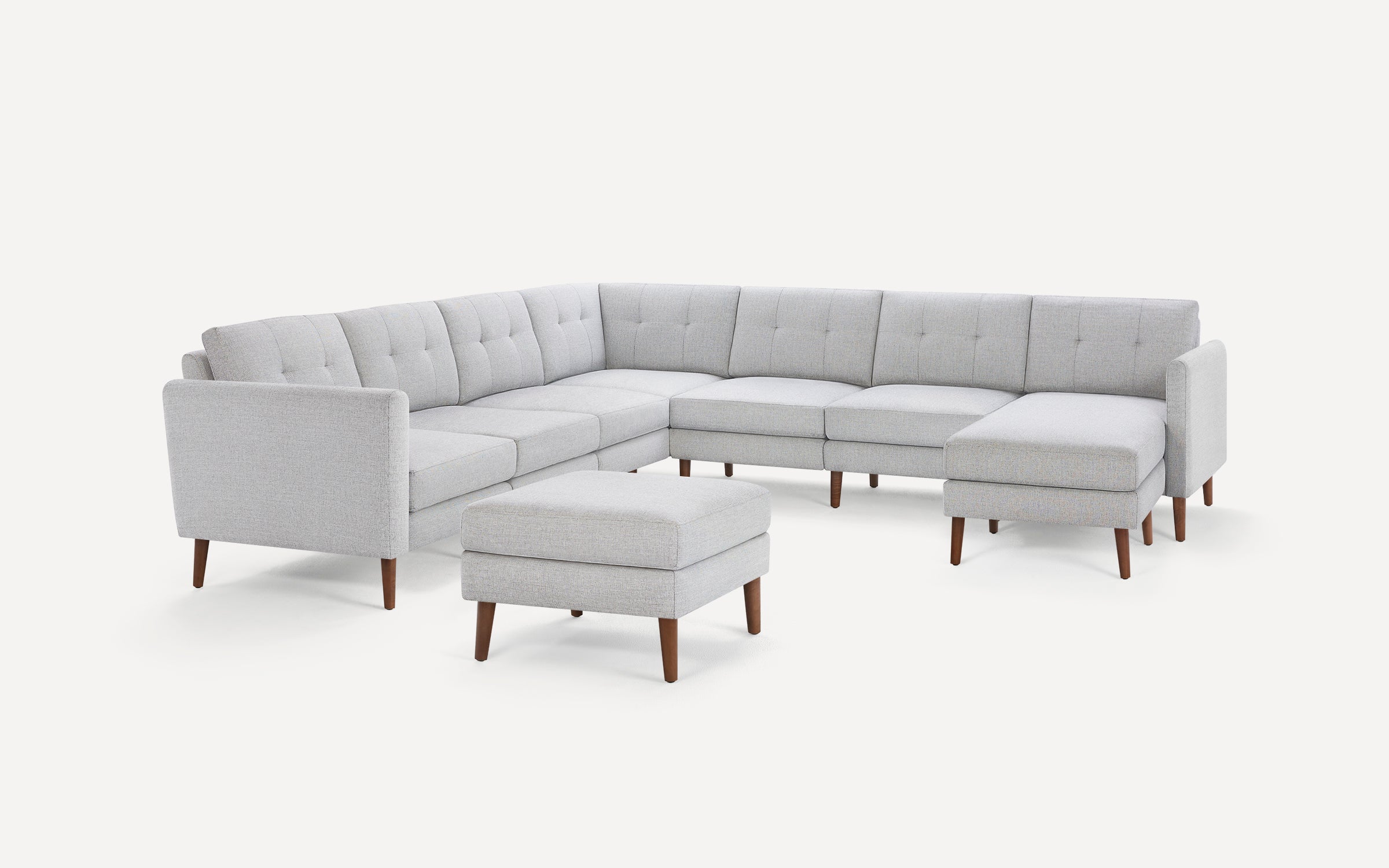 Light gray modern sectional sofa with tufted cushions and wooden legs, paired with a matching ottoman on white background.