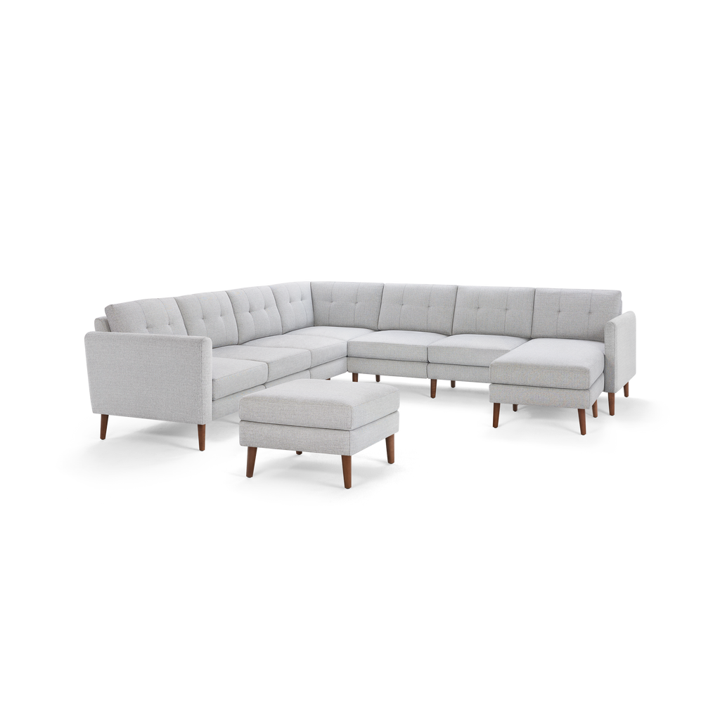 Light grey fabric upholstered sectional sofa with tufted back cushions, wooden tapered legs, and a matching rectangular ottoman.