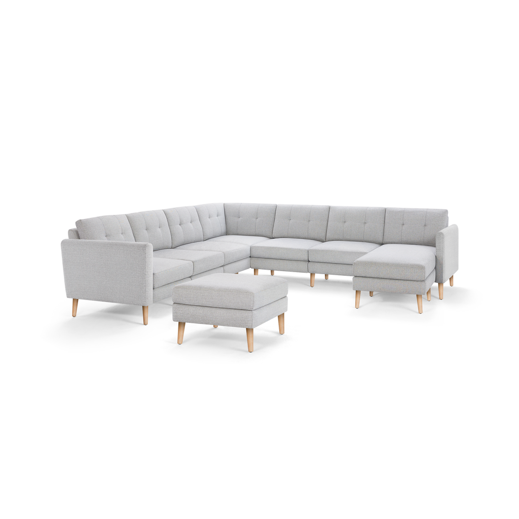 Light grey L-shaped sectional sofa with tufted back cushions and matching ottoman, featuring wooden legs.
