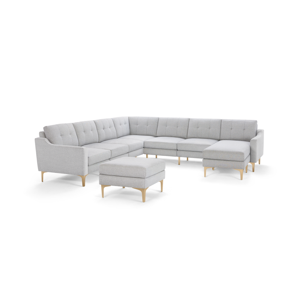 Light gray fabric sectional sofa with tufted back cushions and wooden legs, featuring a matching ottoman.