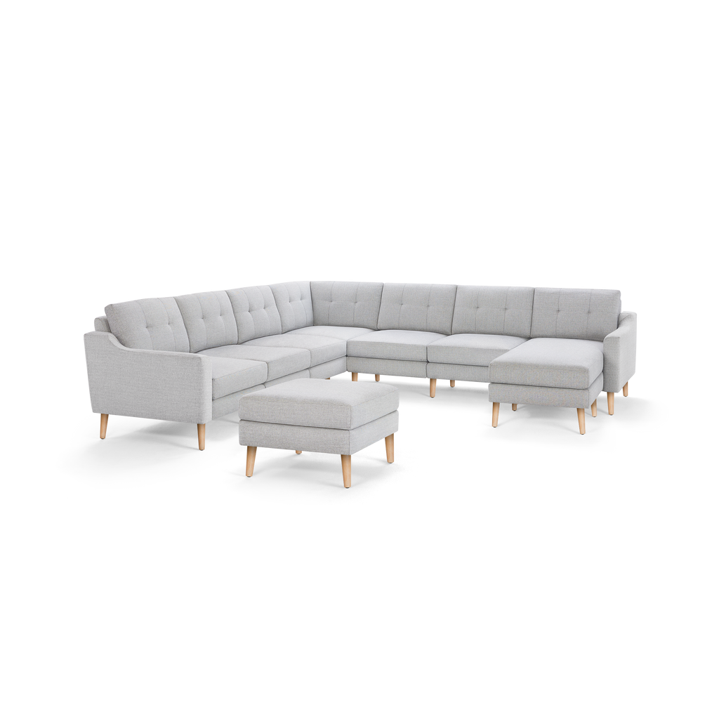 Light gray L-shaped sectional sofa with tufted cushions and light wooden legs, accompanied by a matching ottoman.
