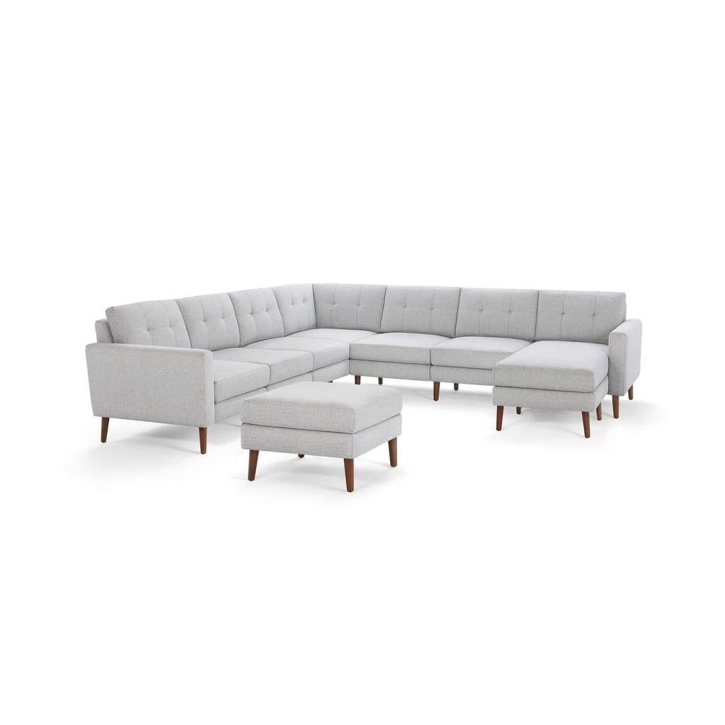Light gray fabric sectional sofa with tufted back cushions, wooden legs, and matching ottoman, modern mid-century design.