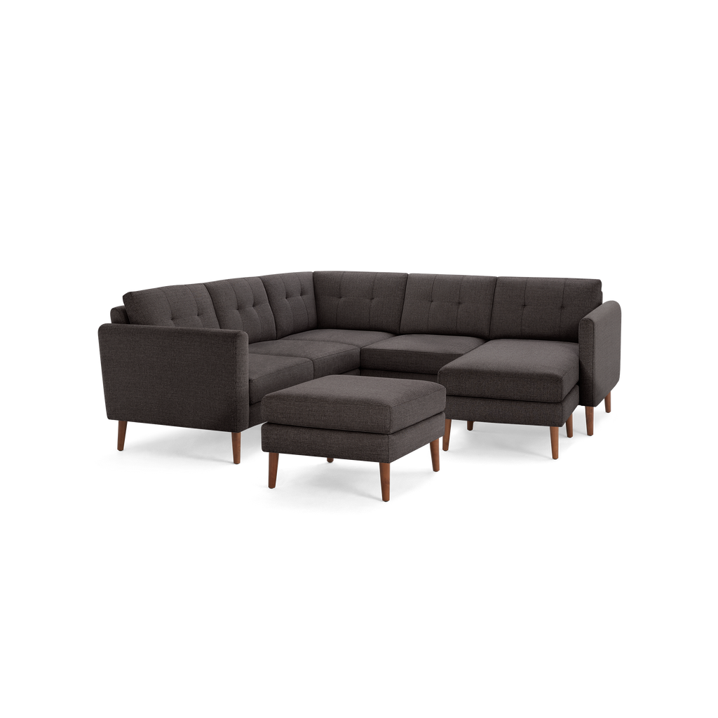 Dark gray fabric sectional sofa with tufted cushions, wooden legs, and a matching ottoman, featuring an L-shaped design.