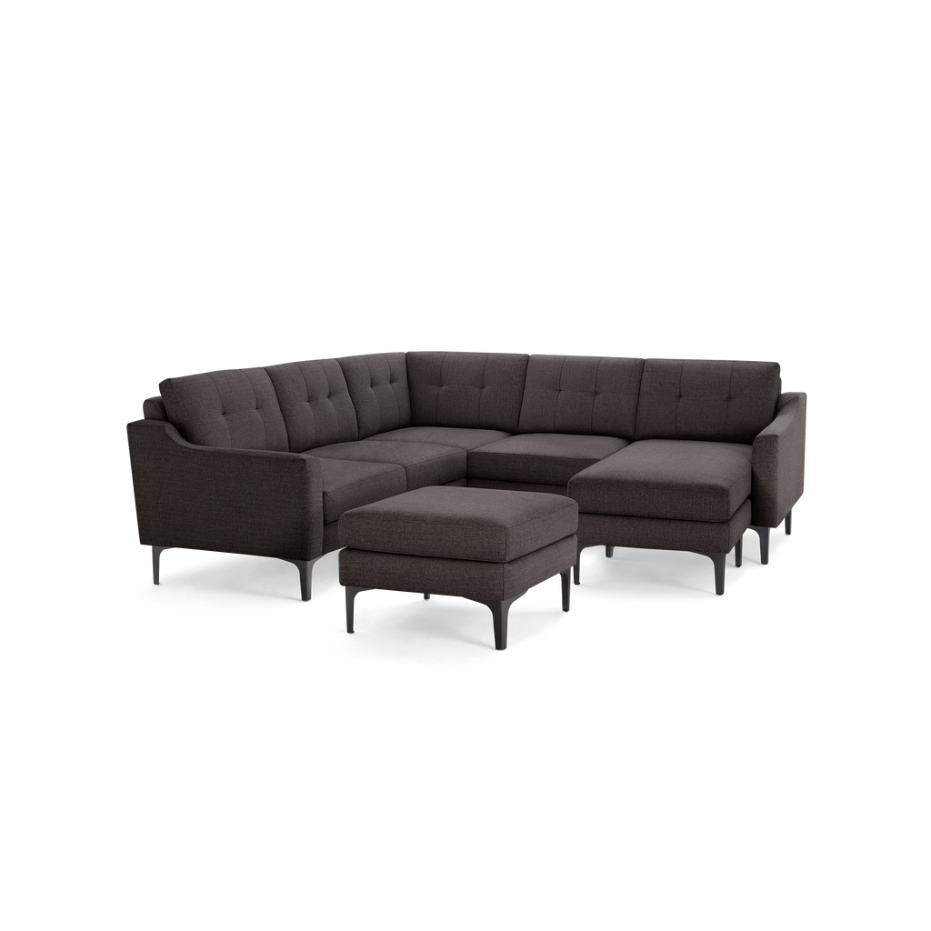 Dark gray fabric sectional sofa with tufted back cushions, angled armrests, chaise lounge, and matching ottoman on black legs.