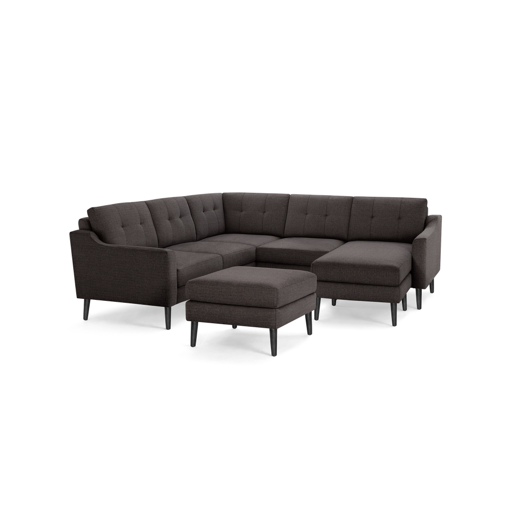 Dark gray fabric L-shaped sectional sofa with tufted back cushions and matching ottoman, supported by black tapered legs.