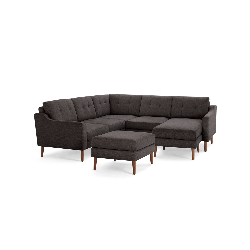 Dark gray upholstered sectional sofa with tufted back cushions, wooden tapered legs, and a matching ottoman.