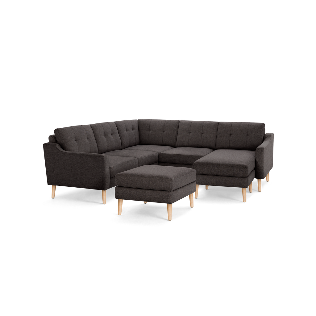 Dark gray fabric sectional sofa with tufted back cushions, wooden legs, and a matching ottoman, isolated on black.