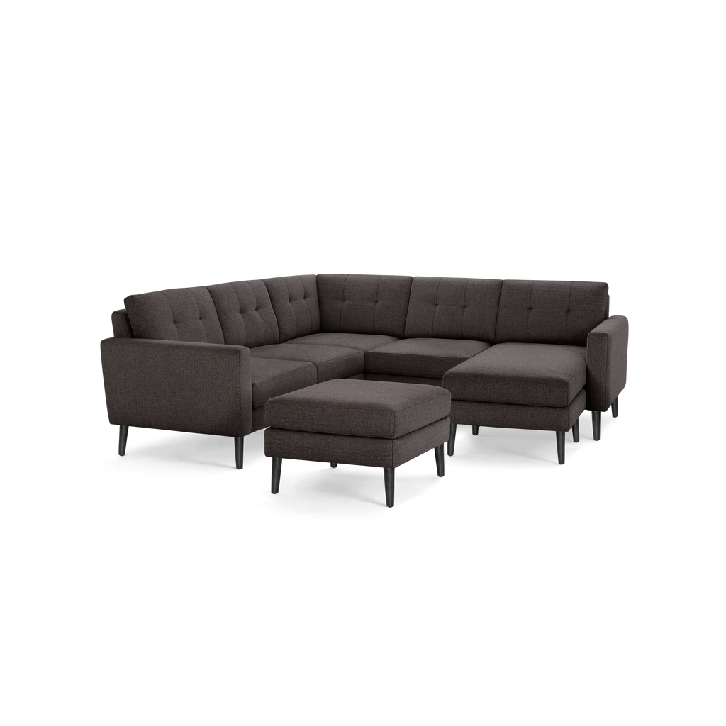 Dark gray tufted fabric sectional sofa with matching ottoman, featuring clean lines and mid-century modern black legs.