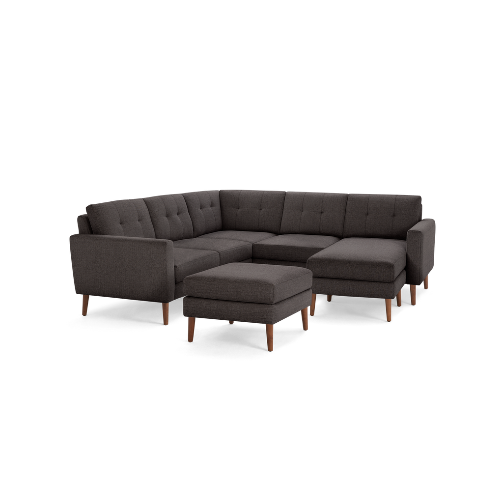 Dark gray fabric L-shaped sectional sofa with tufted cushions and wooden legs, including a matching ottoman.