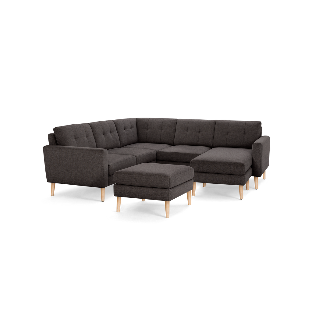 Dark gray fabric L-shaped sectional sofa with tufted cushions and light wooden legs, including a matching ottoman.