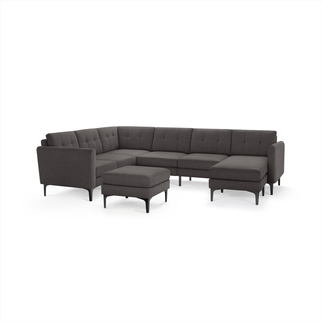 Dark gray fabric upholstered modern modular sectional sofa with tufted back cushions and matching ottoman, supported by slender black legs.