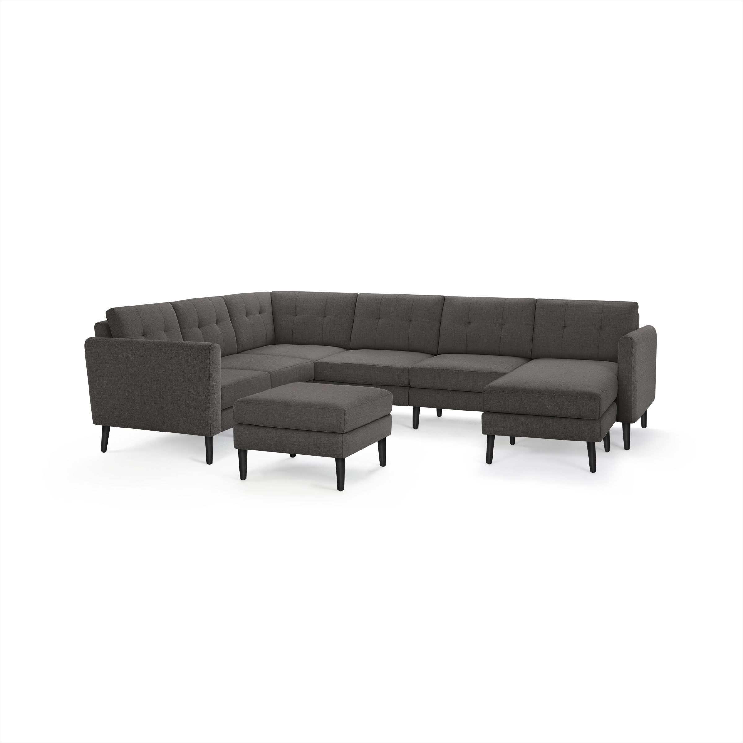 Dark gray modern sectional sofa with tufted cushions, black angled legs, and matching ottoman isolated on white background.