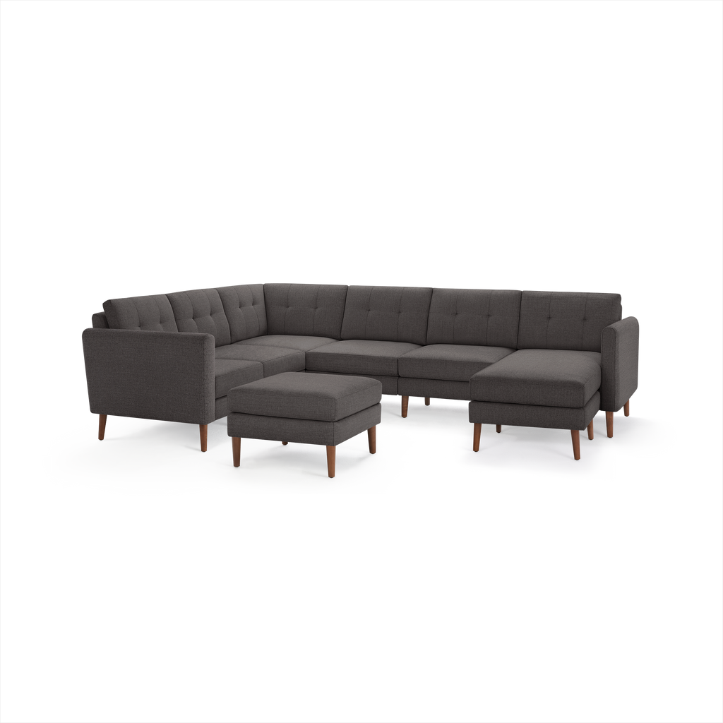 Dark gray L-shaped modern sectional sofa with tufted cushions, wooden legs, and matching ottoman on white background.