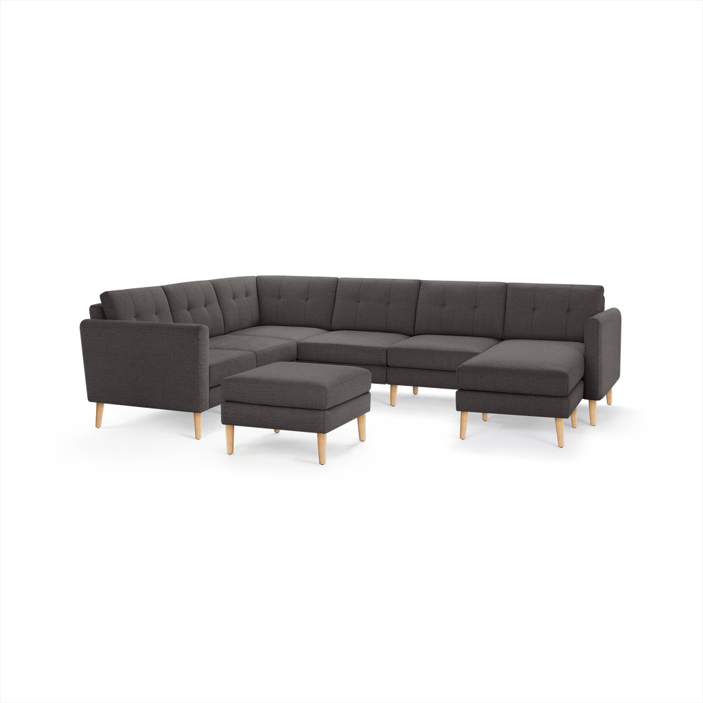 Dark gray fabric sectional sofa with tufted cushions, wooden legs, and matching ottoman, modern mid-century design.