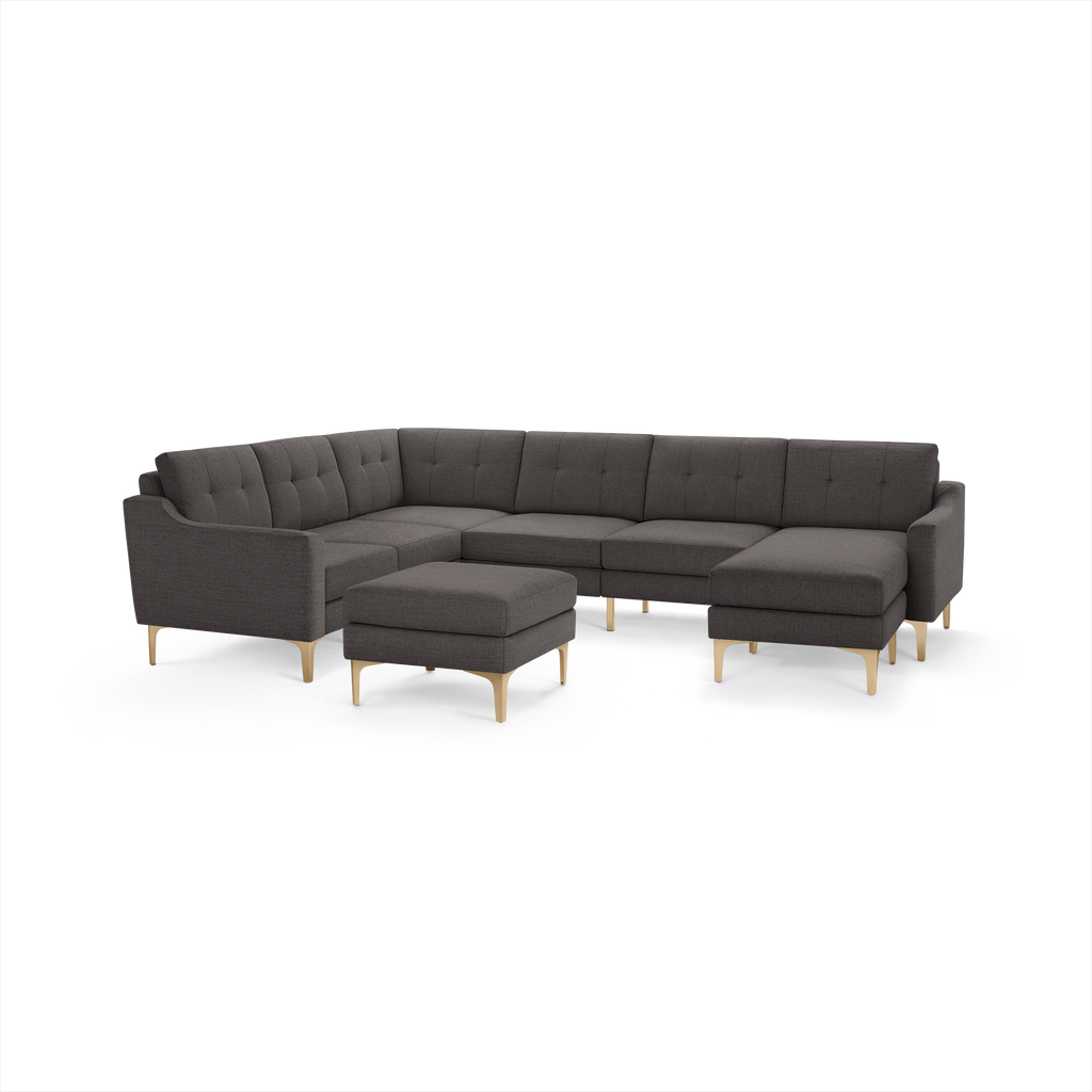 Dark gray L-shaped sectional sofa with tufted cushions, wooden legs, and matching ottoman isolated on white background.
