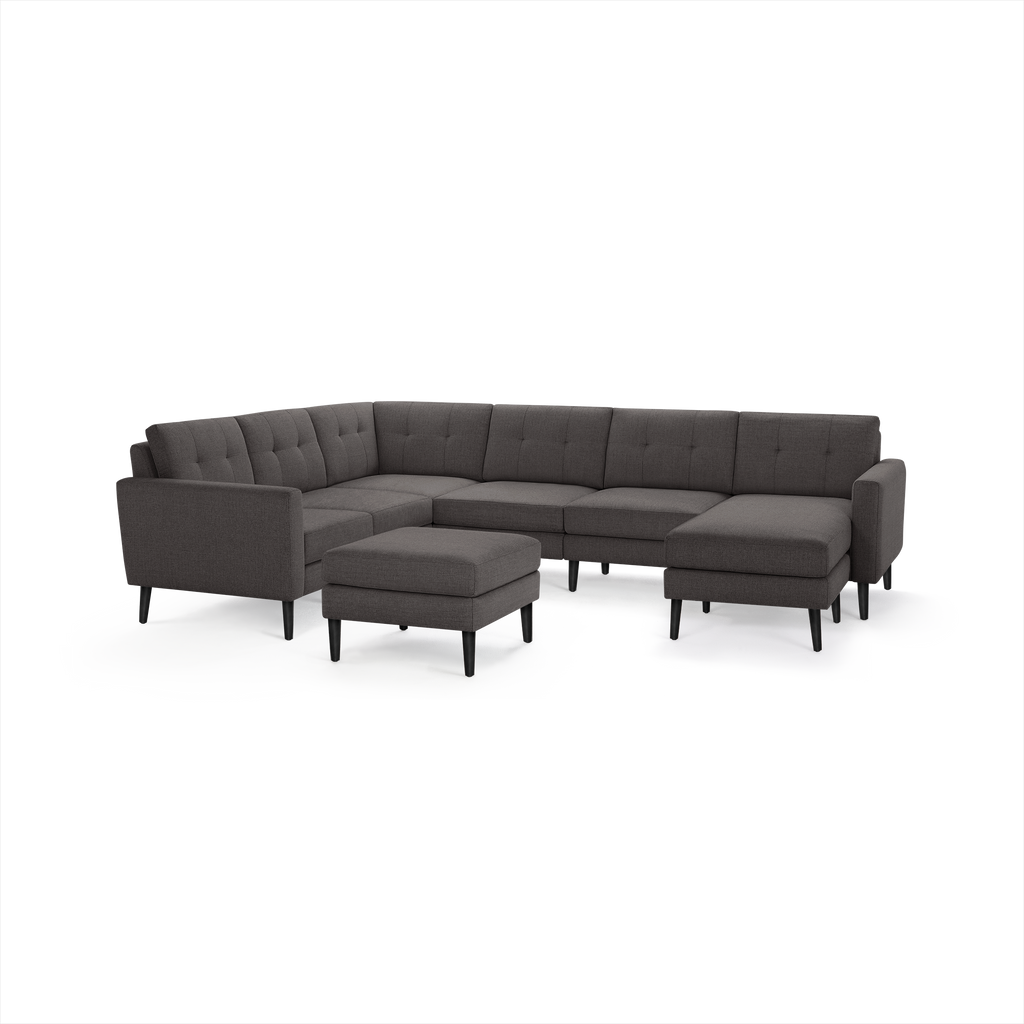 Dark gray fabric sectional sofa with tufted back cushions, sleek armrests, black tapered legs, and matching ottoman.