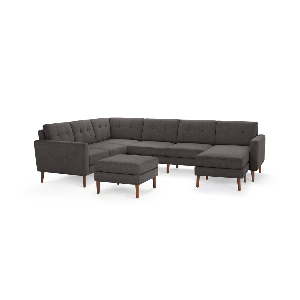 Dark gray upholstered L-shaped sectional sofa with tufted back cushions and wooden legs, accompanied by a matching ottoman.