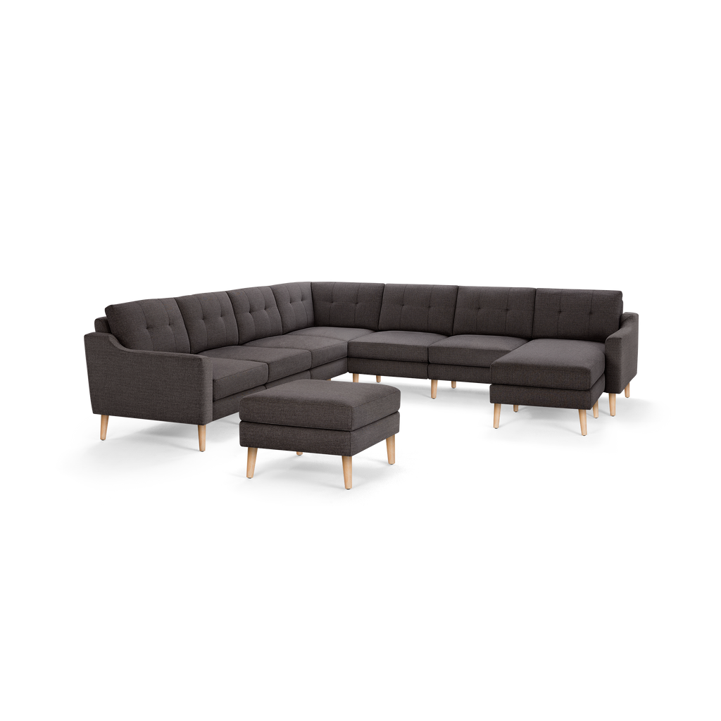 Dark gray L-shaped sectional sofa with button-tufted back cushions and light wooden legs, accompanied by a matching ottoman.
