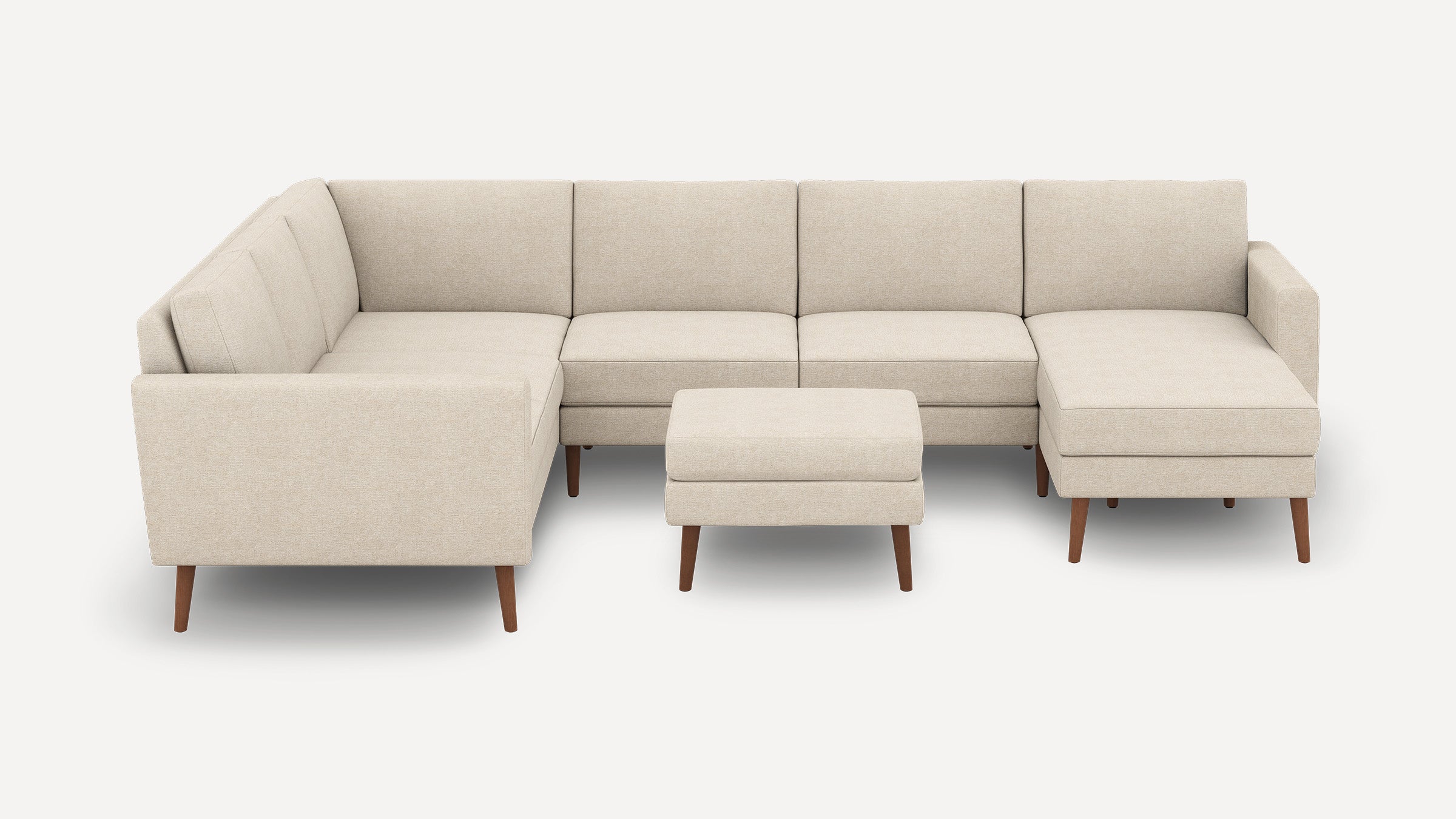 Beige L-shaped sectional sofa with wooden legs, including a matching rectangular ottoman, on a white background.