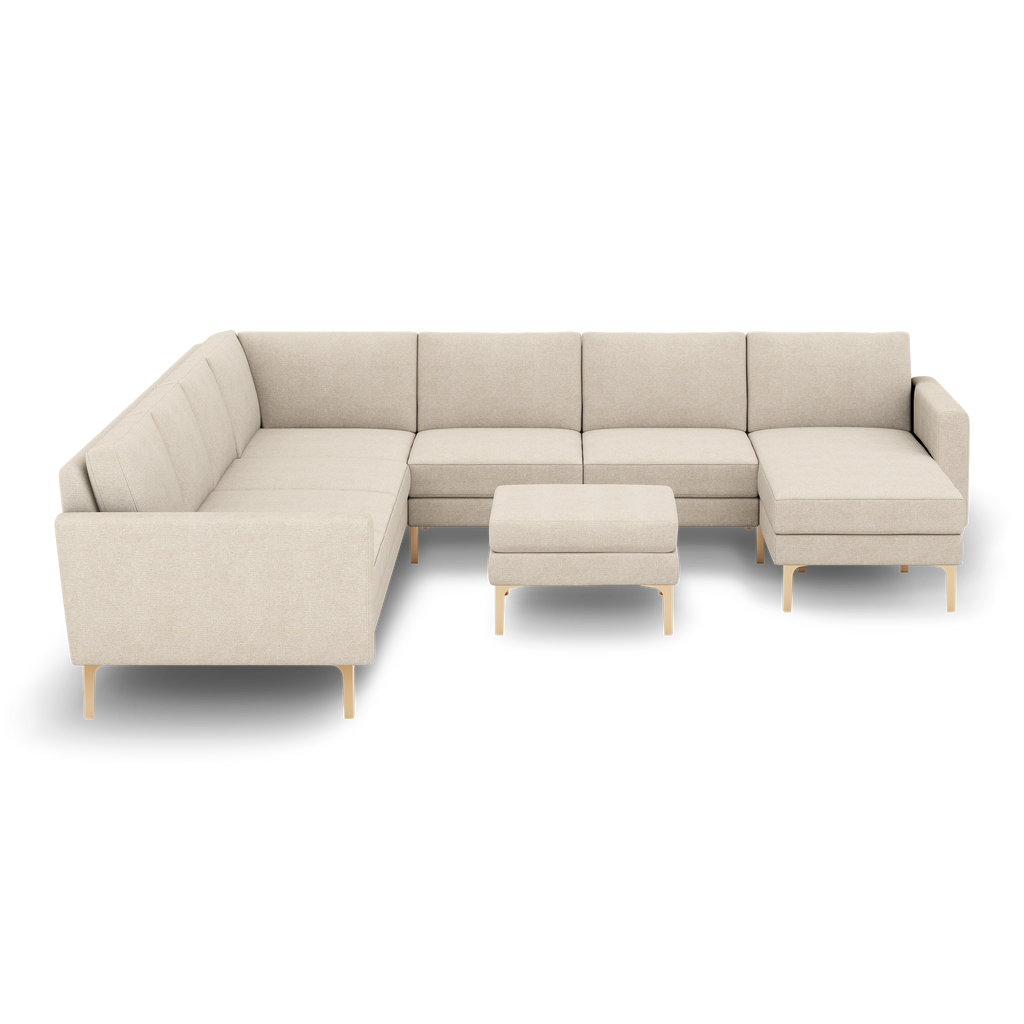 Beige fabric L-shaped sectional sofa with tufted cushions and wooden legs, accompanied by matching square ottoman.