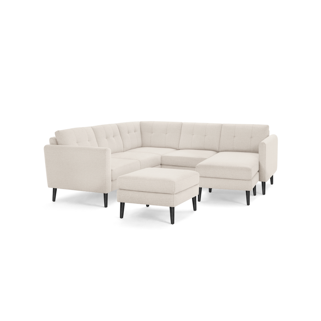 Beige fabric L-shaped sectional sofa with tufted cushions and black tapered wooden legs, including a matching ottoman.