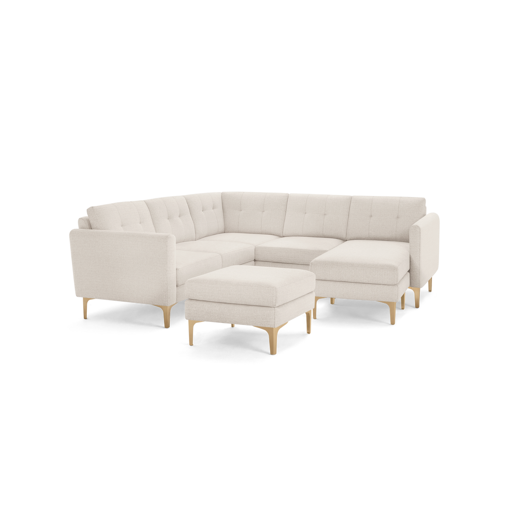 Beige upholstered modern sectional sofa with tufted back cushions, wooden legs, and a matching ottoman on a transparent background.