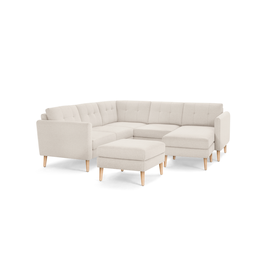 Beige fabric sectional sofa with tufted backrests, wooden tapered legs, and a matching rectangular ottoman against a white background.