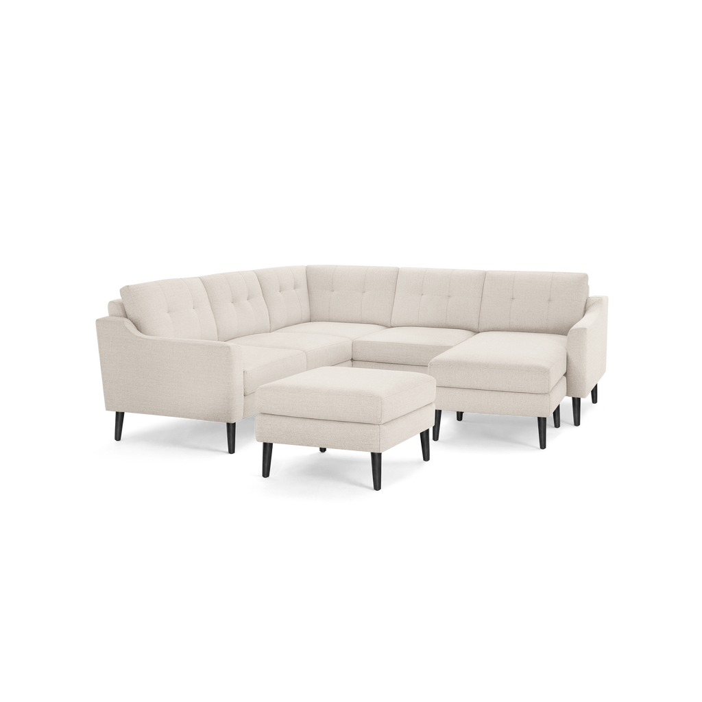 Beige fabric L-shaped sectional sofa with tufted cushions, slim armrests, black wooden legs, and matching ottoman.