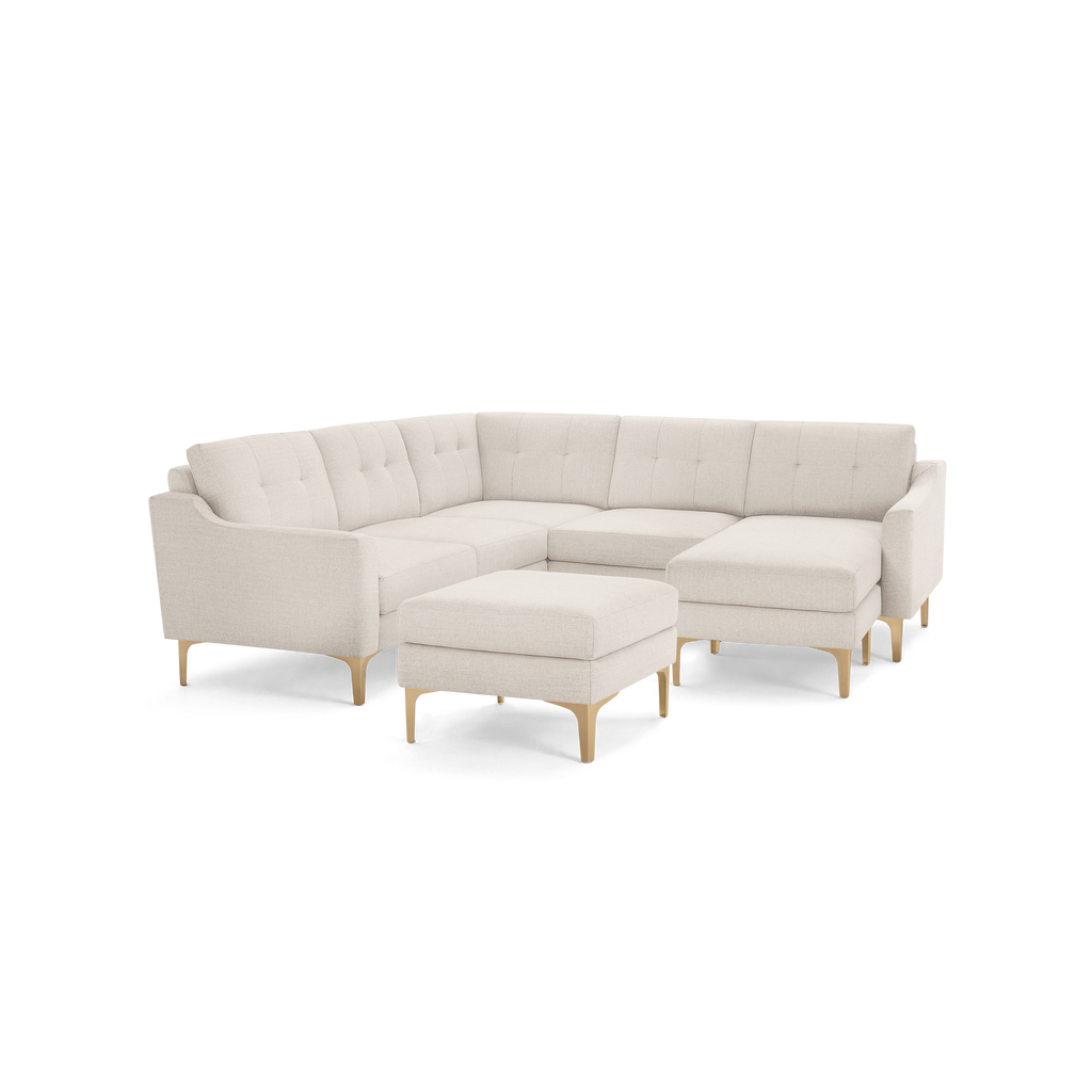 Beige sectional sofa with tufted back cushions, wooden legs, and a matching ottoman, featuring a modern and clean design.