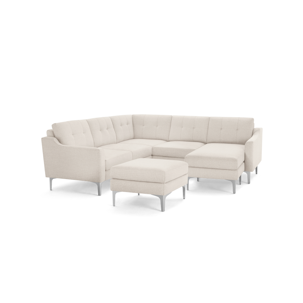 Beige upholstered modern sectional sofa with tufted back cushions, metal legs, and matching ottoman on black background.