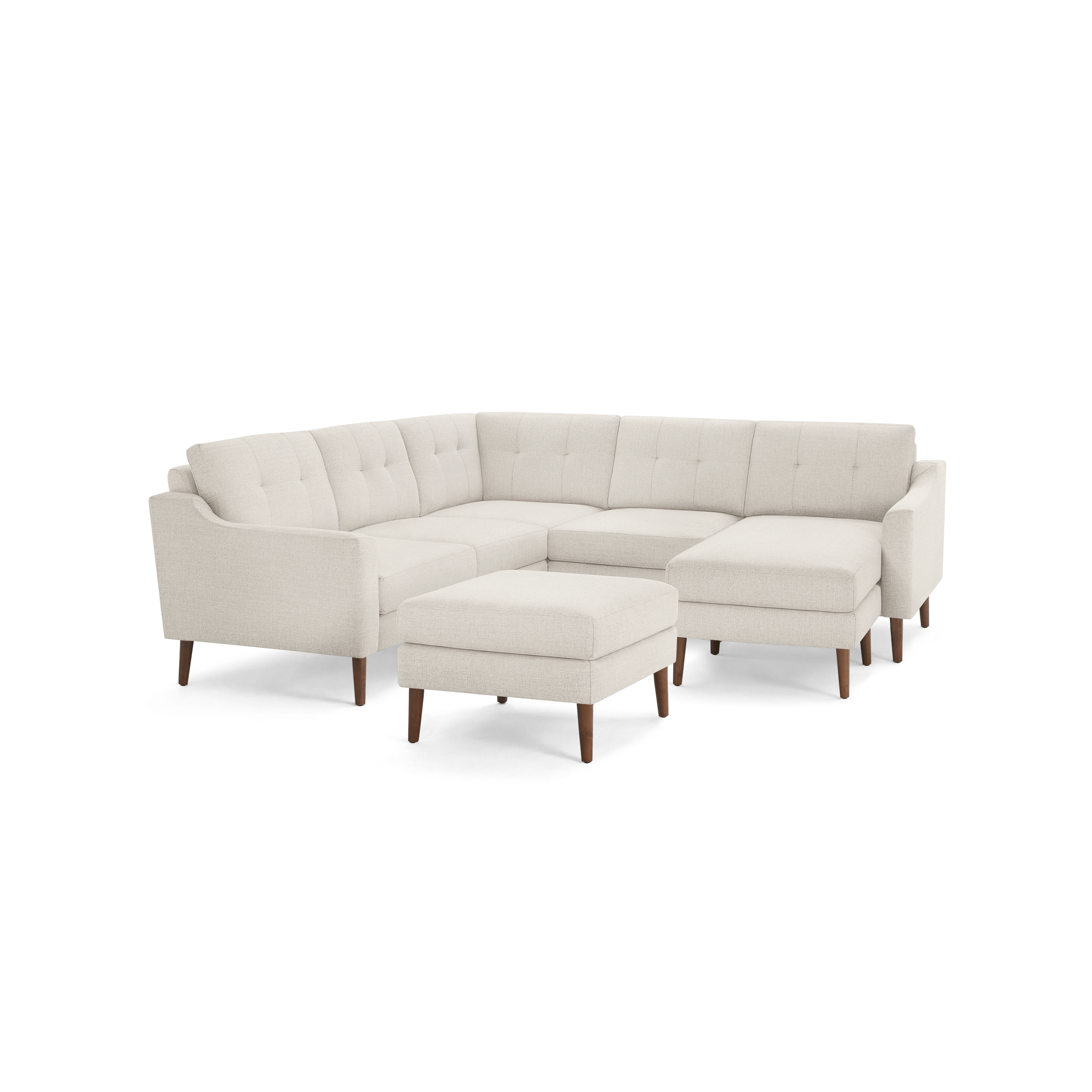 Light beige L-shaped sectional sofa with tufted back cushions, wooden legs, and matching ottoman on a black background.