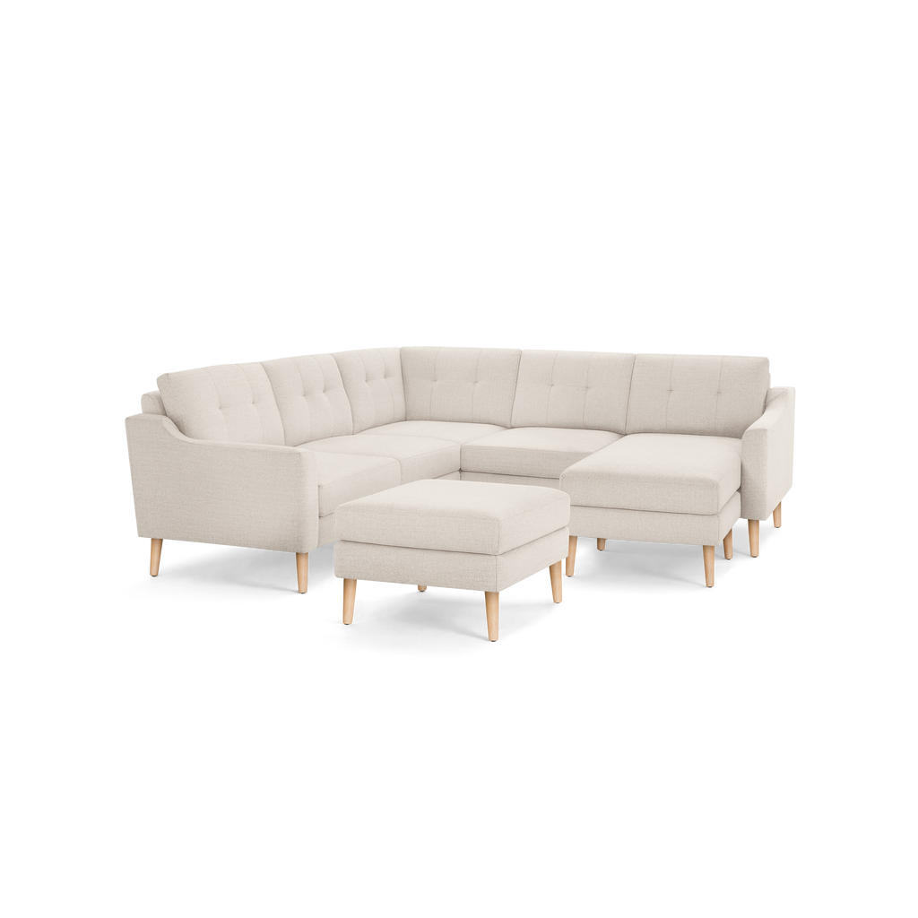 Light beige L-shaped sectional sofa with tufted back cushions, wooden legs, and a matching square ottoman.